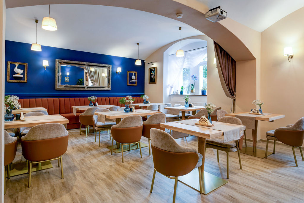 Interi&eacute;r restaurace s modrou st&ecaron;nou, oran&zcaron;ovou &ccaron;aloun&ecaron;nou lavic&iacute; a prost&rcaron;en&yacute;mi stoly s k&rcaron;esly.